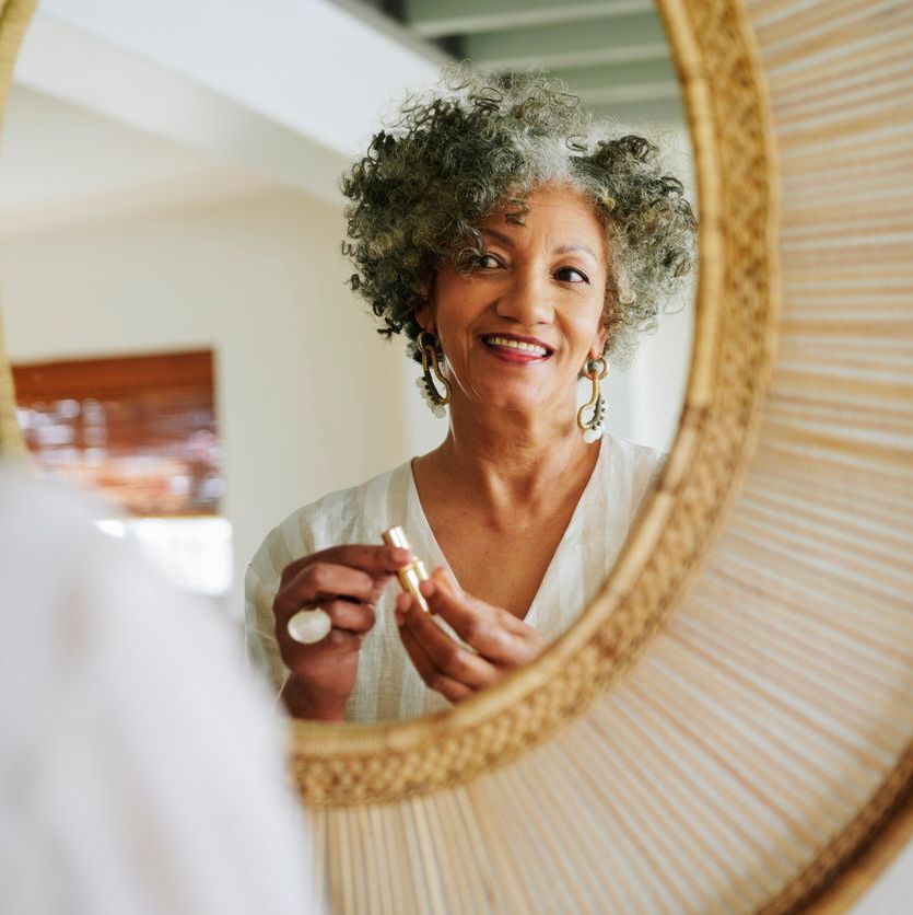 Smiling mature woman putting on lipstick in a mirror at home